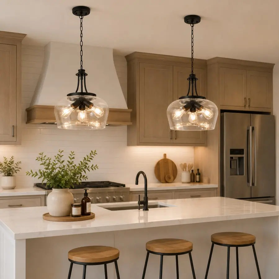 Two black pendant lights with clear glass globes hang over a white kitchen island in a modern kitchen with beige cabinets and stainless steel appliances.