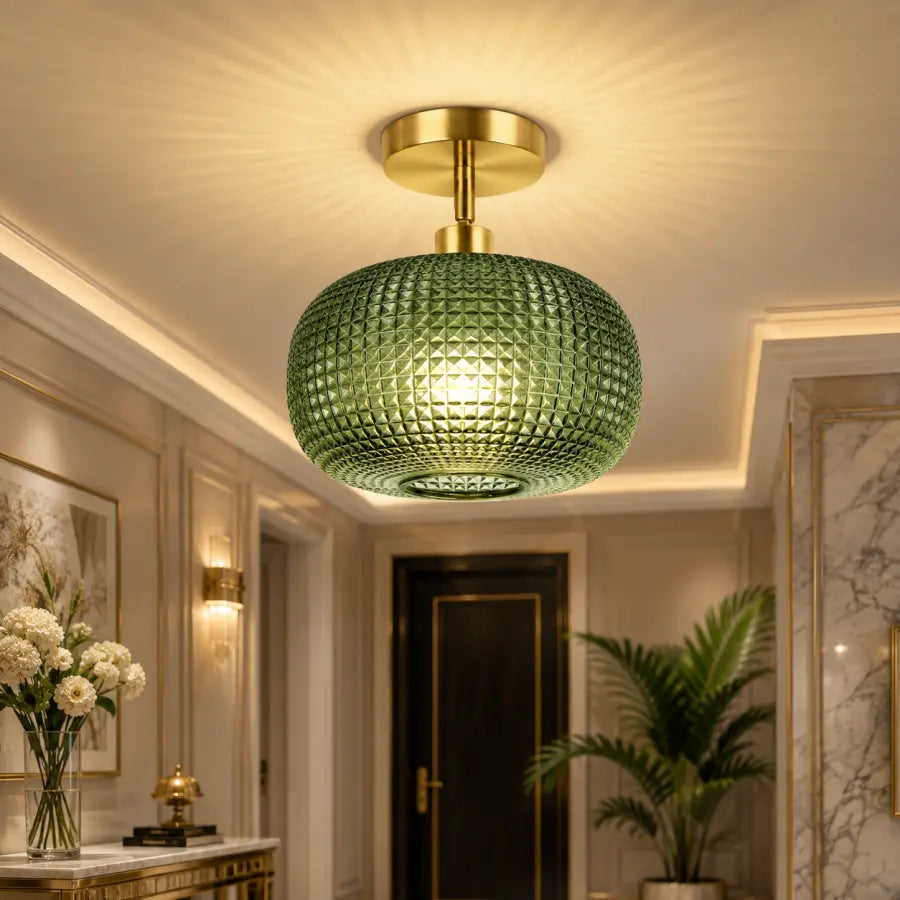 A modern ceiling light fixture with a textured green glass globe shade and a gold-finished ceiling mount, shown installed in a luxurious hallway with warm ambient lighting.