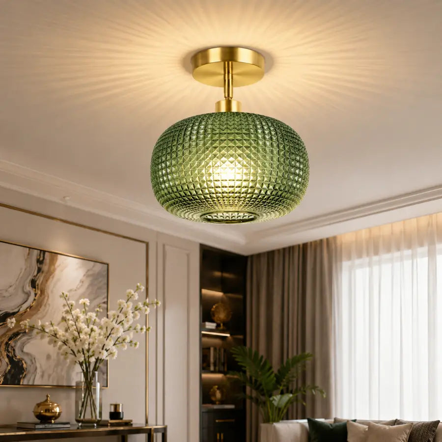A modern semi-flush mount ceiling light with a textured green glass globe shade and a gold brass ceiling canopy, shown installed in a luxurious living room.