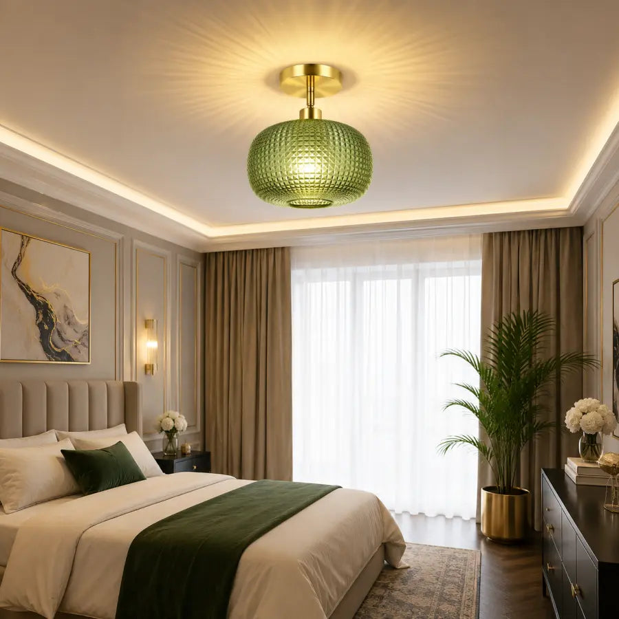 A modern ceiling light fixture with a textured green glass globe shade and a gold brass ceiling mount, shown illuminated in a styled bedroom setting.