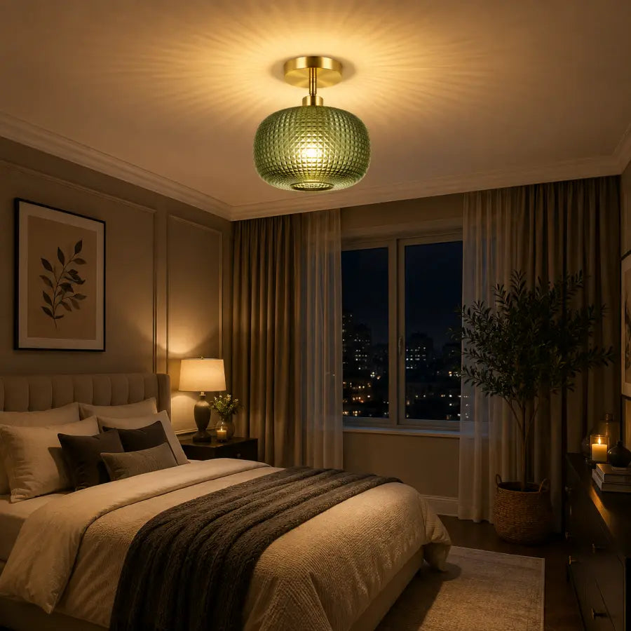 A modern semi-flush mount ceiling light with a textured green glass shade and a gold brass ceiling canopy, glowing in a warm light within a styled bedroom.