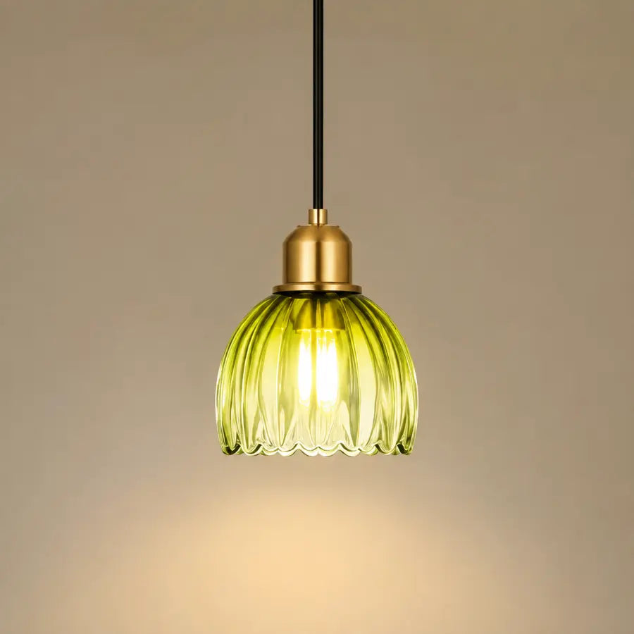 A hanging pendant light with a ribbed translucent yellow-green glass shade, a brass-toned metal cap, and a black cord against a warm beige background.