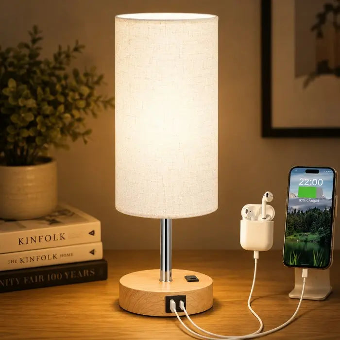 Modern bedside table lamp with USB charging port, 3-way dimmable touch control, linen fabric shade, and wooden base on a bedroom nightstand with warm ambient lighting.