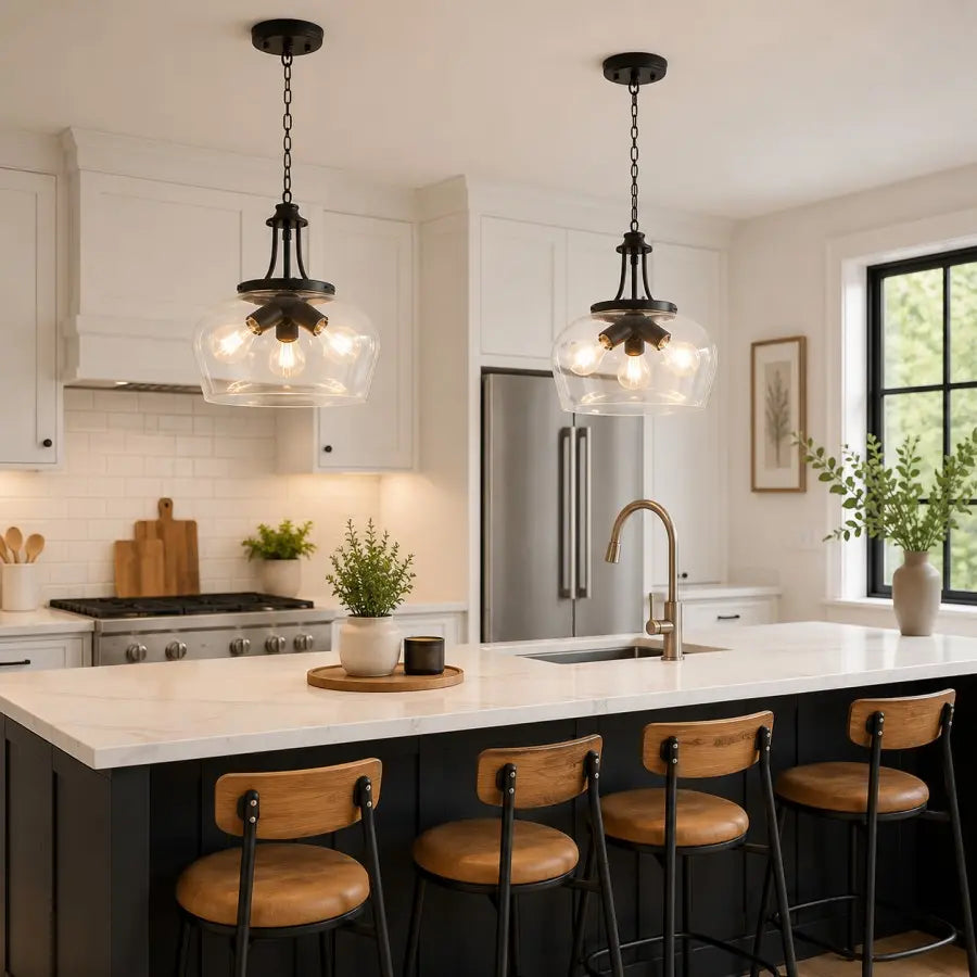 Two black pendant lights with clear glass globes hang over a white kitchen island in a bright modern kitchen with white cabinets, a stainless steel refrigerator, and wooden bar stools.