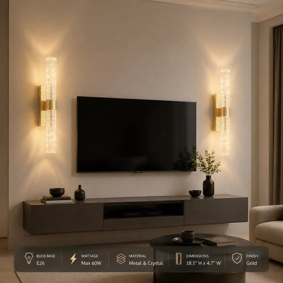 A pair of modern wall sconces with vertical crystal-like glass tubes and gold accents, mounted on either side of a wall-mounted TV above a dark media console in a living room setting.